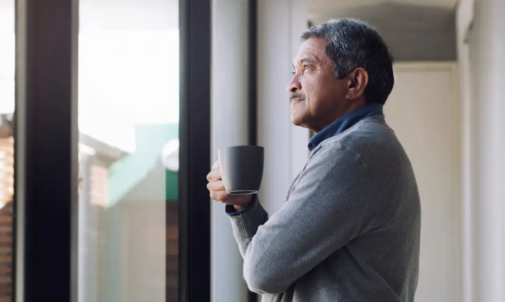 senior man sipping hot drink looking out window