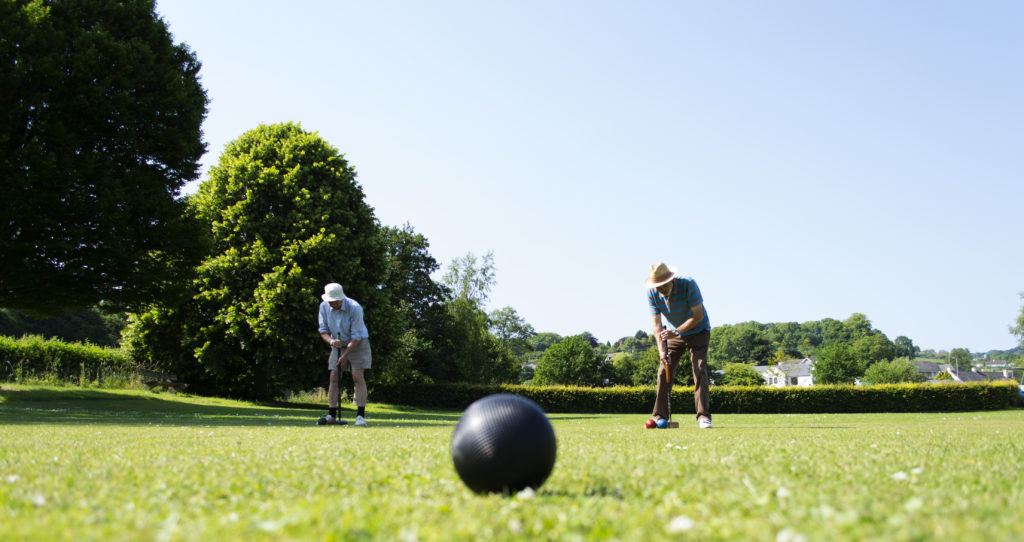 Two men in hats playing croquet, with a closeup of a black croquet ball