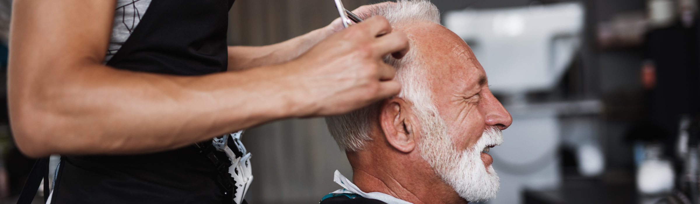 White-haired man getting a hair cut in a barber shop