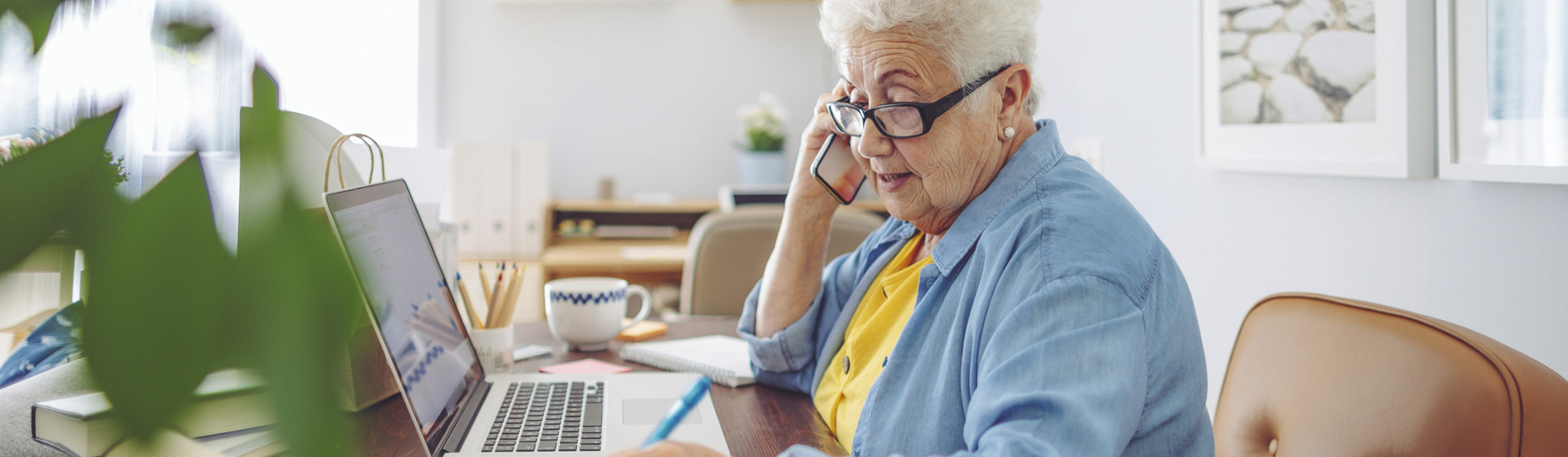 Older woman talking on her cellphone and paying her bills at her laptop