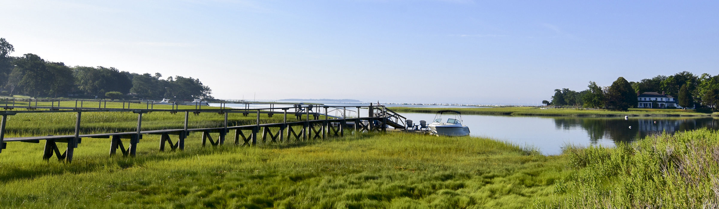 Wooden walkway across lush grasses down to a boat in the water