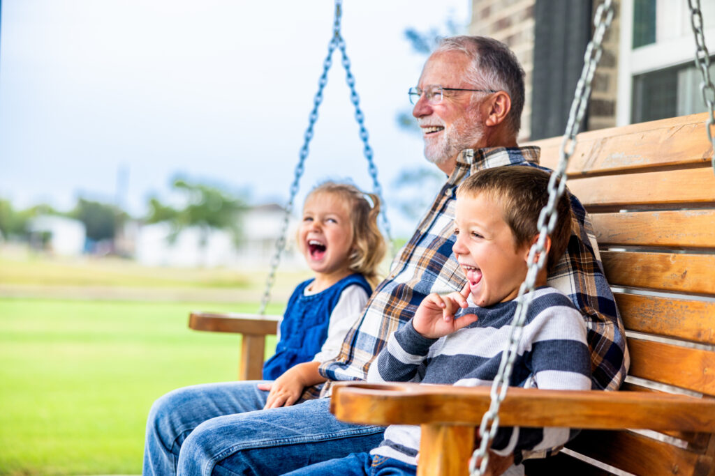 Grandfather with grandchildren on a porch swing, laughing together