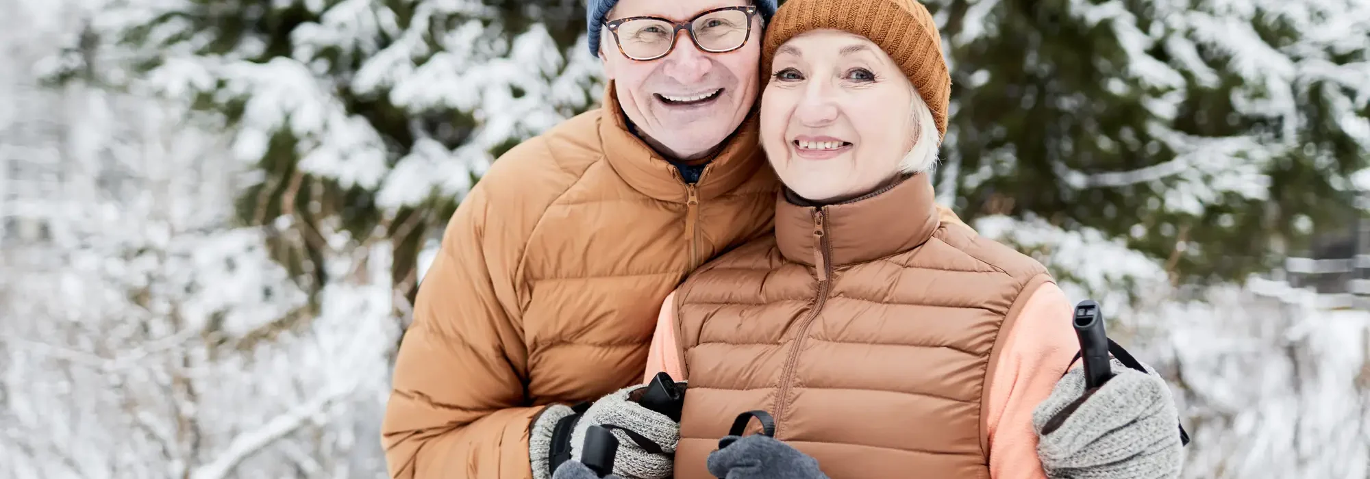 Senior couple in winter gear outside in front of a snowy pine