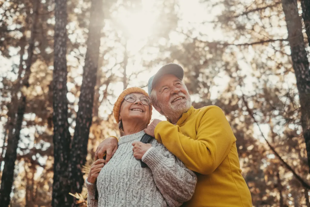 Head shot portrait close up of middle age cheerful people smiling and looking at the the trees of the forest around them. Active couple of old seniors hiking and walking together in the mountain having fun.