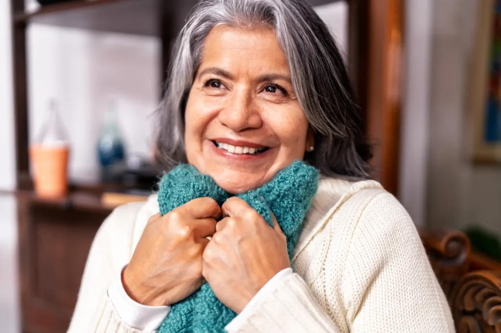 Portrait of a smiling senior woman holding a knitted shawl, enjoying the warmth and comfort of her handmade craft