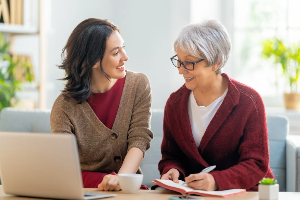Adult daughter and senior woman taking notes, looking at laptop, and talking about moving to assisted living in Duxbury, Massachusetts.