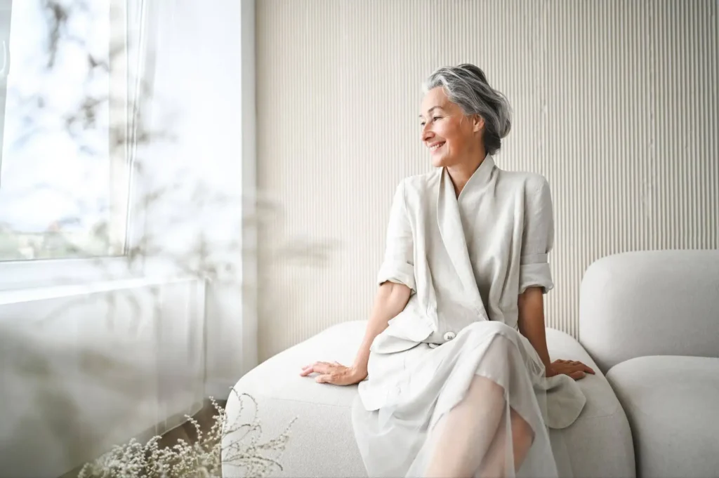 A senior woman sitting on her bed considering downsizing for retirement to move to The Village at Duxbury for maintenance-free living.