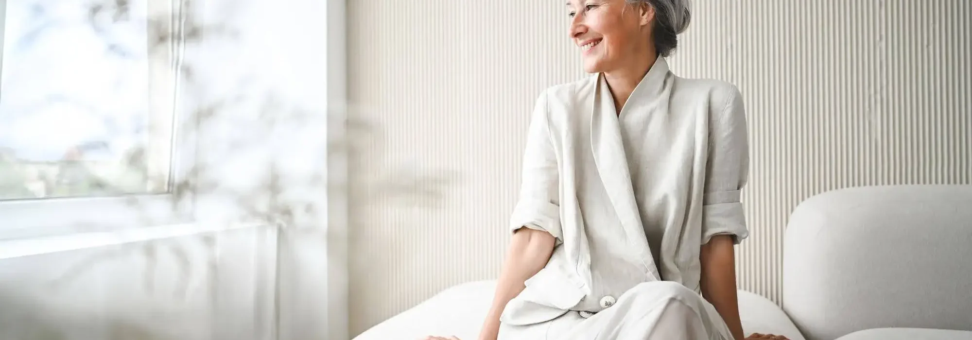 A senior woman sitting on her bed considering downsizing for retirement to move to The Village at Duxbury for maintenance-free living.
