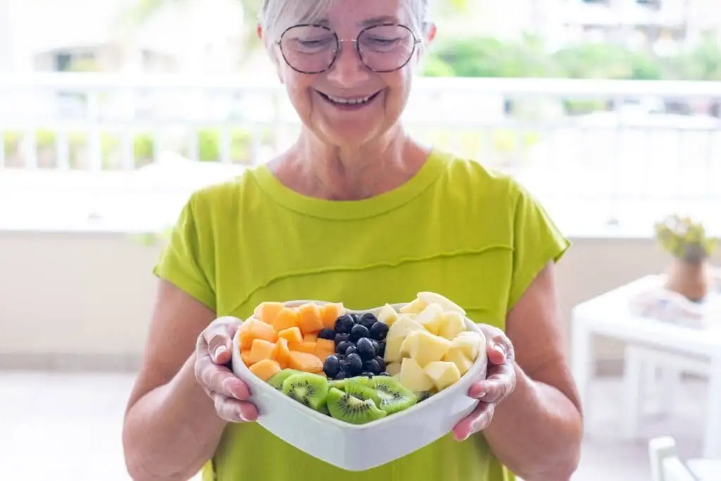 Best Senior Living Options for Heart Health Support: A Guide for Seniors & Families 2 An elderly woman holding a bowl of fruit from her home at The Village at Duxbury, a senior living community that offers heart health support in Duxbury MA.